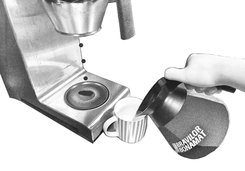 Kahvikuppi on pöydällä kahvinkeittimen vieressä kun siihen kaadetaan kahvia. Tippoja tippuu kahvinkeittimen suodatinkorista sen lämmityslevylle.